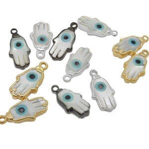 May include: Assortment of gold, silver, and black hamsa hand charms with blue evil eye details. The charms are made of metal and have a white shell inlay.