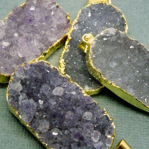 以下が含まれることがあります： 金メッキの縁取りが施されたアメジストクリスタルのペンダントが4つ。クリスタルは薄い紫色で、ざらざらとした自然な質感です。