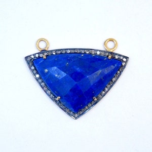 Puede incluir: Un colgante triangular con una gran piedra preciosa de lapislázuli azul rodeada por un borde de pequeños diamantes. El colgante tiene dos anillos de salto de oro para sujetar una cadena.