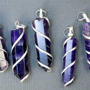 May include: Six amethyst crystal pendants wrapped in silver wire. The pendants are all different sizes and shapes, but they are all a deep purple color.