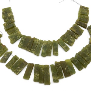 May include: Two strands of olive green jade beads, each composed of rectangular, roughly cut pieces. The beads are strung on thin, dark threads, and the background is plain white. The jade has a natural, earthy appearance.