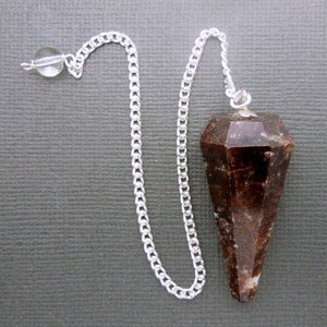 Op de afbeelding: Een bruin en wit kristallen slinger met een zilveren ketting en een helder kristal aan de bovenkant.