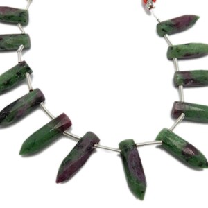 May include: A strand of green and pink gemstone beads, each bead is shaped like a pointed bullet. The beads are strung on a silver wire.