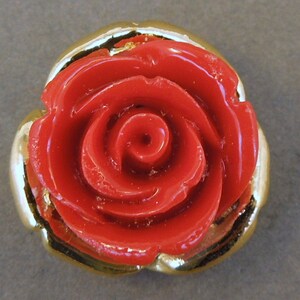May include: A red rose button with a gold trim. The rose is three-dimensional and has a glossy finish.
