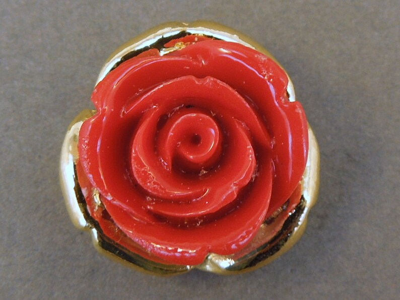 May include: A red rose button with a gold trim. The rose is three-dimensional and has a glossy finish.