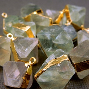 May include: A group of green fluorite gemstone pendants with gold accents. Each pendant is a faceted, geometric shape with a gold bail.