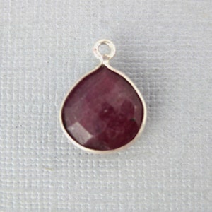 May include: A teardrop-shaped pendant with a red gemstone set in silver.