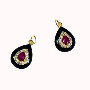 May include: Two gold-tone teardrop-shaped pendants with black enamel and a red rhinestone in the center. Each pendant is surrounded by a halo of smaller clear rhinestones.