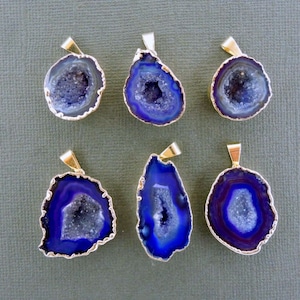 May include: Six blue and white geode pendants with gold-colored metal trim. The pendants have a natural, irregular shape and a gold-colored bail for hanging. The geodes have a crystalline interior.