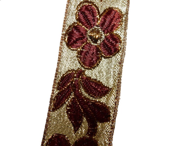 May include: Gold and burgundy trim with a floral design. The trim features a repeating pattern of flowers and leaves.