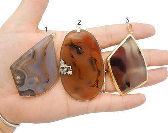 May include: Three agate pendants with gold-tone settings. The pendants are in the shapes of a diamond, oval, and a rectangle. The agate is brown, white, and gray with a swirling pattern.