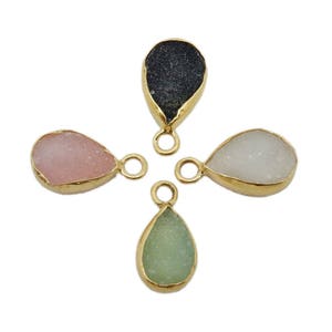 May include: Four teardrop-shaped gemstone pendants with gold-tone settings. The gemstones are black, pink, white, and green.