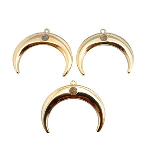 Op de afbeelding: Drie gouden halvemaan-bedels met een heldere steen in het midden van elke maan.