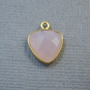Puede incluir: Un colgante dorado con una piedra preciosa triangular de color rosa claro.