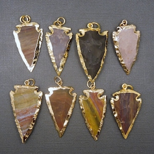 May include: Eight gold-plated arrowhead pendants with different colored agate stones. The arrowheads are all the same size and shape, but each has a unique pattern of colors and textures.