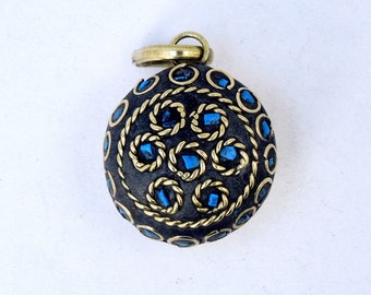 May include: A round, black pendant with a gold-colored design and blue gemstones. The pendant has a loop at the top for attaching to a chain.