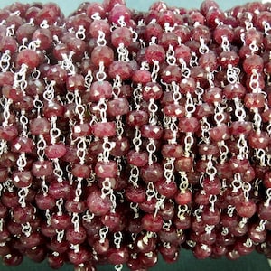 May include: A close-up of a ruby gemstone chain, featuring faceted red beads and silver chain links. The chain is perfect for jewelry making or crafting.