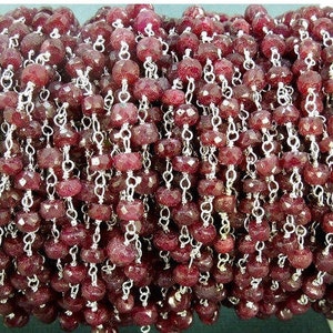 May include: A close-up of a ruby red gemstone chain, featuring faceted beads and silver chain links. The chain is perfect for jewelry making or crafting.