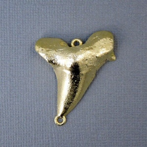 May include: Gold-tone shark tooth pendant with a loop at the top for hanging and a loop at the bottom for attaching to a chain.
