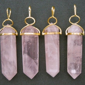 May include: Four rose quartz crystal pendants with gold-toned wire wraps. The pendants are all the same size and shape, and they are hanging from a grey background.