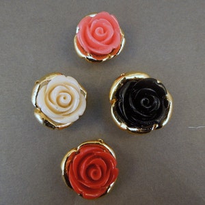 May include: Four decorative rose-shaped buttons with gold settings. The roses are in pink, white, black, and red.