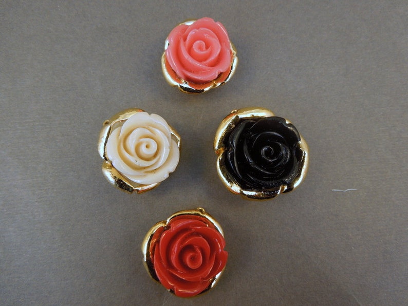May include: Four decorative rose-shaped buttons with gold settings. The roses are in pink, white, black, and red.