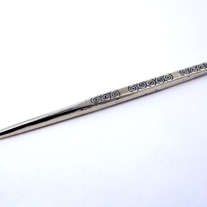 May include: A silver-colored, pointed tool with a decorative pattern of concentric circles along the shaft.