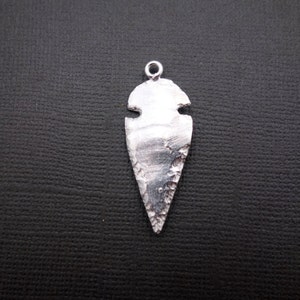 Puede incluir: Encanto de colgante de punta de flecha de plata con una superficie texturizada.