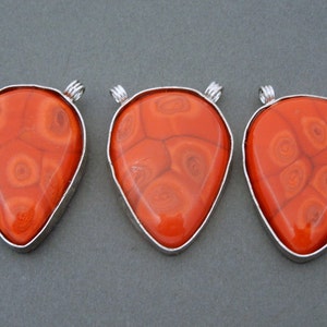 May include: Three orange agate teardrop pendants with silver wire wraps. The agate has a swirling pattern.