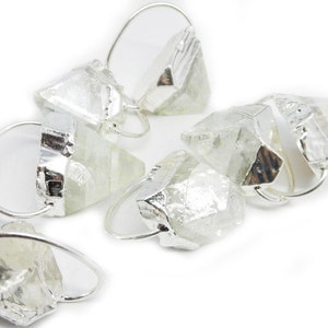 Puede incluir: Un conjunto de seis anillos de cristal transparente con engastes de plata. Los anillos tienen forma de pirámide con una punta puntiaguda y una base plana. Los anillos son de diferentes tamaños y formas.