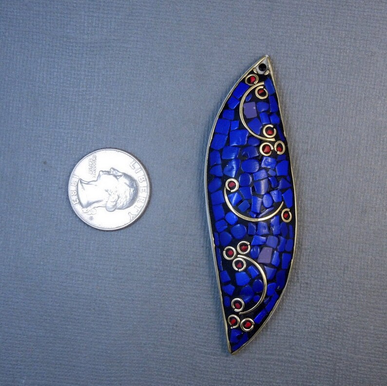 Op de afbeelding: Een blauwe en gouden hanger met een moza&iuml;ekontwerp. De hanger heeft de vorm van een traan en heeft rode accenten.