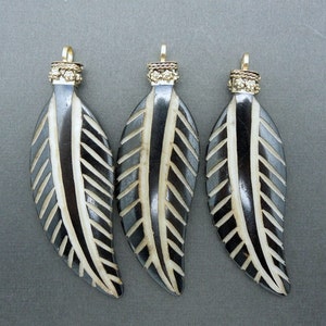 May include: Three black and white carved bone leaf pendants with gold-toned metal bails. The leaves have a geometric pattern and are approximately 2 inches long.