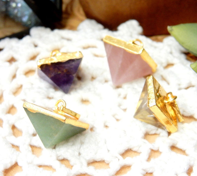 K&ouml;nnte beinhalten: Vier goldumrandete pyramidenf&ouml;rmige Kristallanh&auml;nger. Die Kristalle sind Amethyst, Rosenquarz, klarer Quarz und gr&uuml;ner Aventurin.