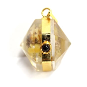 May include: A gold-toned pendant with a clear, faceted crystal containing small pieces of yellow and brown material. A black gemstone is set in the center of the pendant.