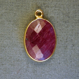 May include: A gold-toned pendant featuring a faceted ruby gemstone in an oval shape.