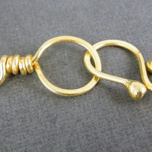 May include: Gold-toned metal clasp with a round loop and a hook. The clasp is designed for attaching jewelry or other items.