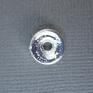 Può includere: Un perno di metallo color argento con un foro al centro. Il perno ha una superficie liscia e lucida.