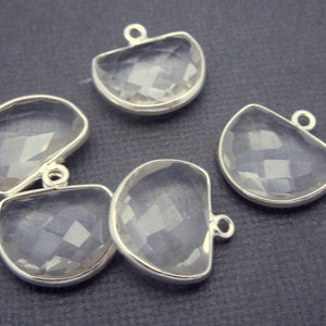 Puede incluir: Cinco colgantes de piedra preciosa de cuarzo transparente con engastes de plata. Cada colgante tiene forma de semicírculo y tiene un pequeño bucle en la parte superior para sujetarlo a una cadena o cordón.