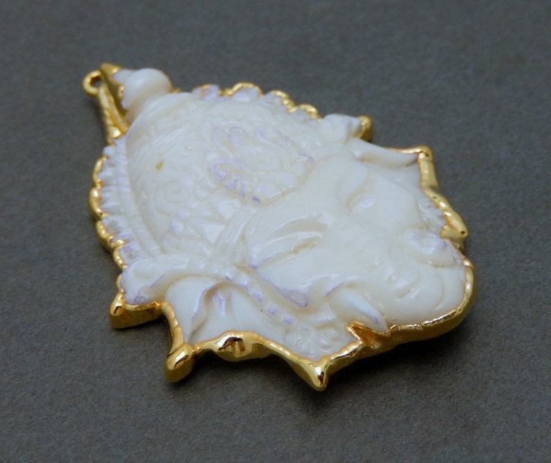 Op de afbeelding: Witte gegraveerde hanger met een gouden rand, met een gedetailleerd gezichtsontwerp.