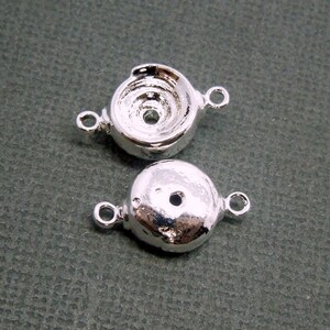 Può includere: Due cappucci per perline in metallo argentato di forma rotonda con un piccolo foro al centro. Ogni cappuccio ha un anello su entrambi i lati per il fissaggio ai gioielli.