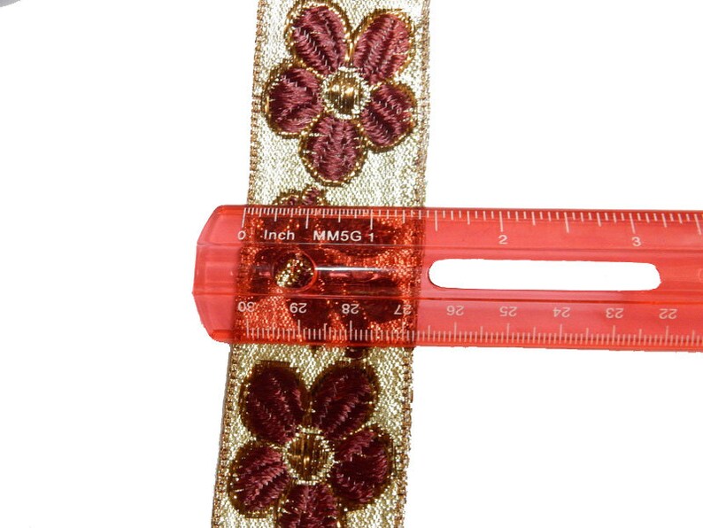 May include: Gold and burgundy floral trim with a ruler measuring 1 inch (2.5 cm) in length.