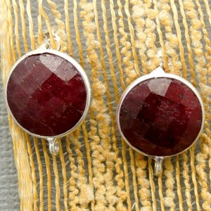 May include: Two round, red ruby gemstone beads with silver bezels and jump rings. The beads are faceted and have a shiny finish.