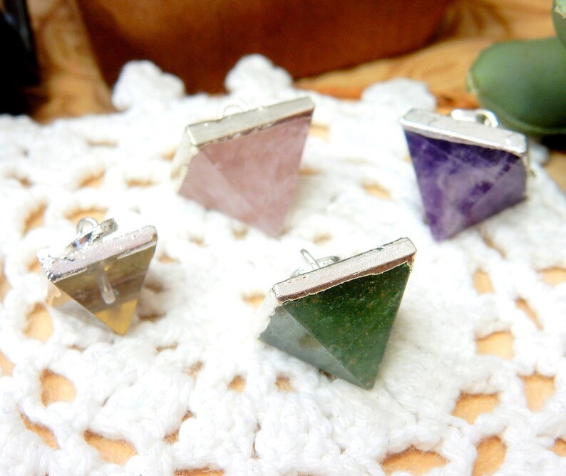 K&ouml;nnte beinhalten: Vier silberne pyramidenf&ouml;rmige Anh&auml;nger mit verschiedenen farbigen Edelsteinen. Die Anh&auml;nger sind aus Silber und haben eine glatte, polierte Oberfl&auml;che. Die Edelsteine sind rosa, lila, gr&uuml;n und braun.