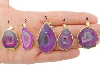 May include: Five purple agate pendants with gold trim. Each pendant has a different shape and size. The pendants are arranged in a row on a hand.