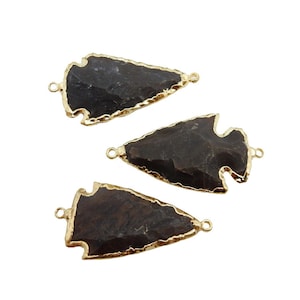 Op de afbeelding: Drie bruine pijlpuntvormige hangers met goudkleurige randen en springringen.