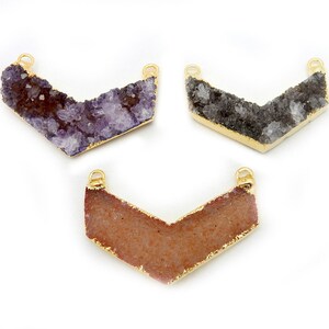 Puede incluir: Tres colgantes de flecha de ágata con borde dorado. Los colgantes son en tonos morado, gris y rosa.