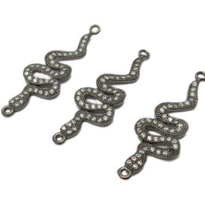 Puede incluir: Tres abalorios de serpiente plateados con detalles de cristal transparente. Cada abalorio tiene un bucle en la parte superior para sujetarlo a joyas.