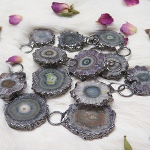 May include: A collection of amethyst crystal pendants with silver-toned metal accents. The crystals are various shades of purple, white, and green, with a unique, swirling pattern.