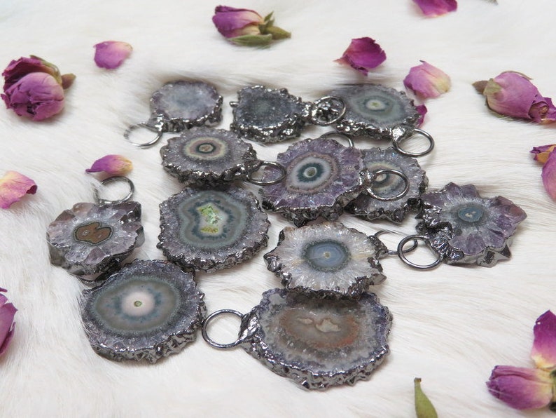 May include: A collection of amethyst crystal pendants with silver-toned metal accents. The crystals are various shades of purple, white, and green, with a unique, swirling pattern.