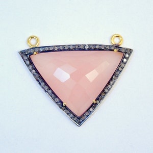 Puede incluir: Un colgante triangular rosa con un marco plateado y un borde de pequeños diamantes. El colgante tiene un aro de oro.